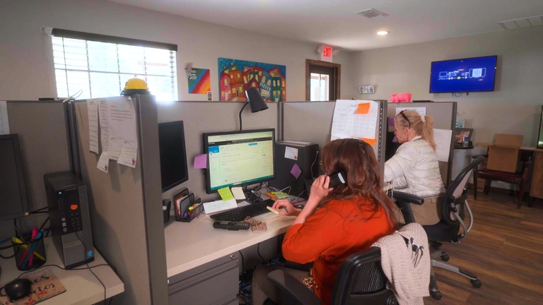 Office environment with two women working at desks, one on a phone call and the other at a computer, highlighting customer service for air conditioning installation at Tillman's Services.